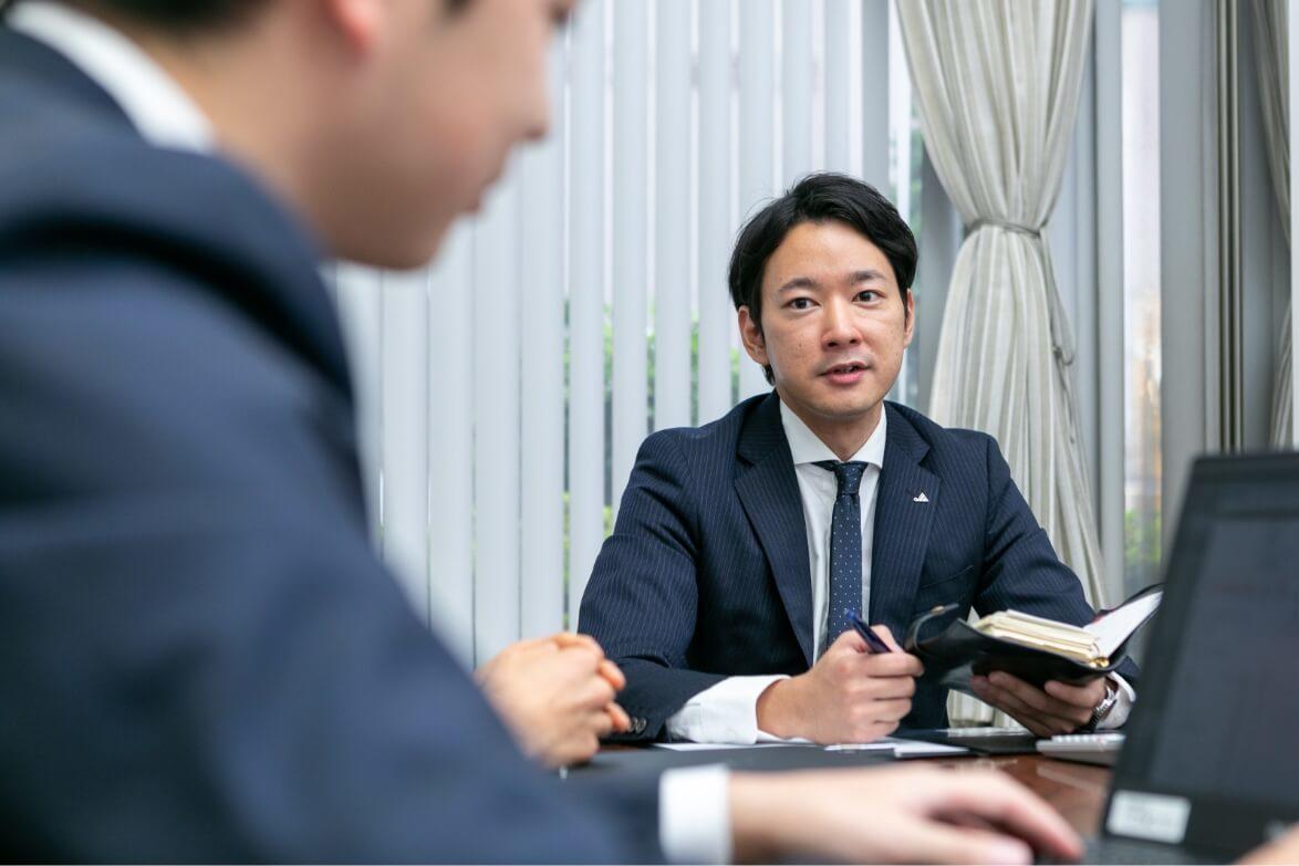 会議でノートを片手に部下に話しかける長野県信連法人融資の男性職員