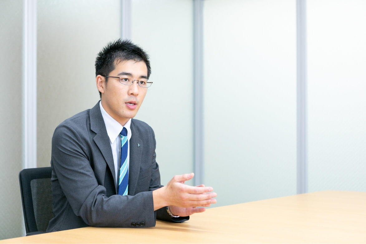 デスクに座りながらインタビューに答える長野県信連証券運用の男性職員
