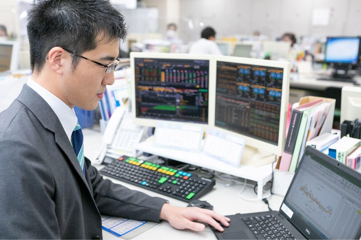 3台のパソコンモニターを前に、座りながらレートチェックをする長野県信連証券運用の男性職員