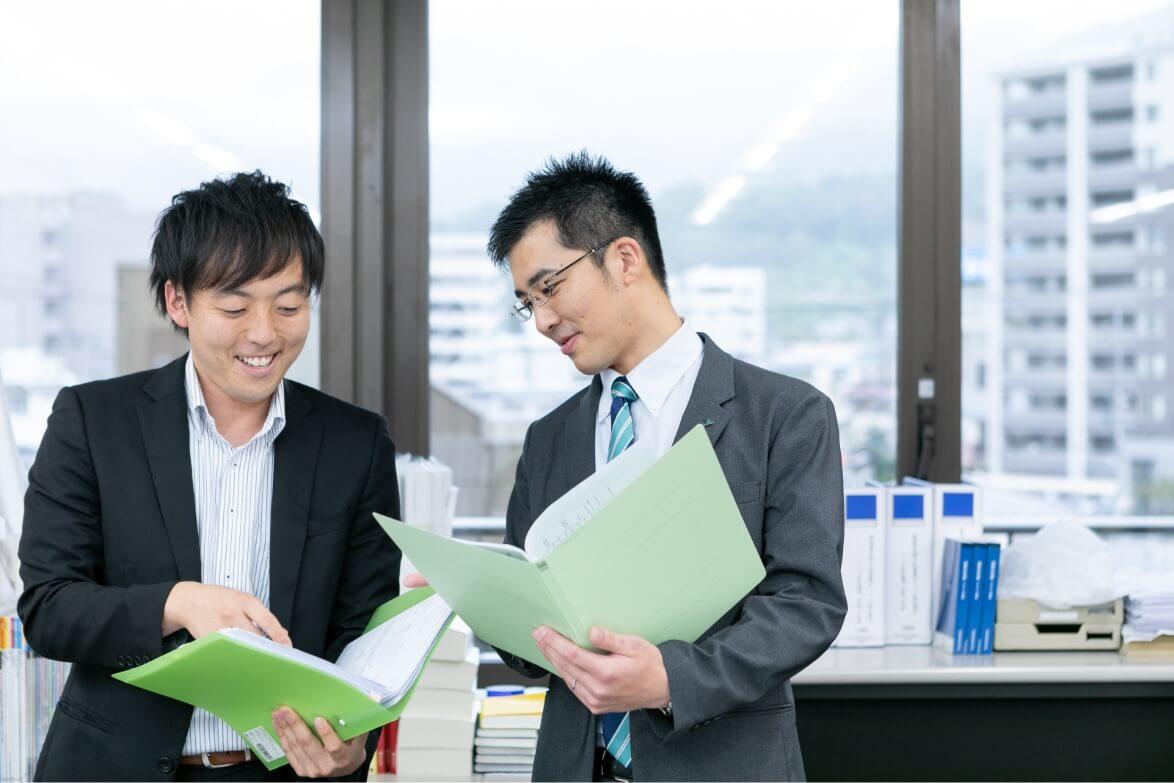 立ちながらファイルを広げ、男性職員と打ち合わせをする長野県信連証券運用の男性職員