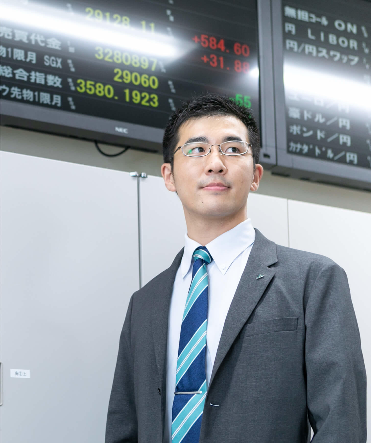 為替レート電光掲示板を背景に立つ長野県信連証券運用の男性職員