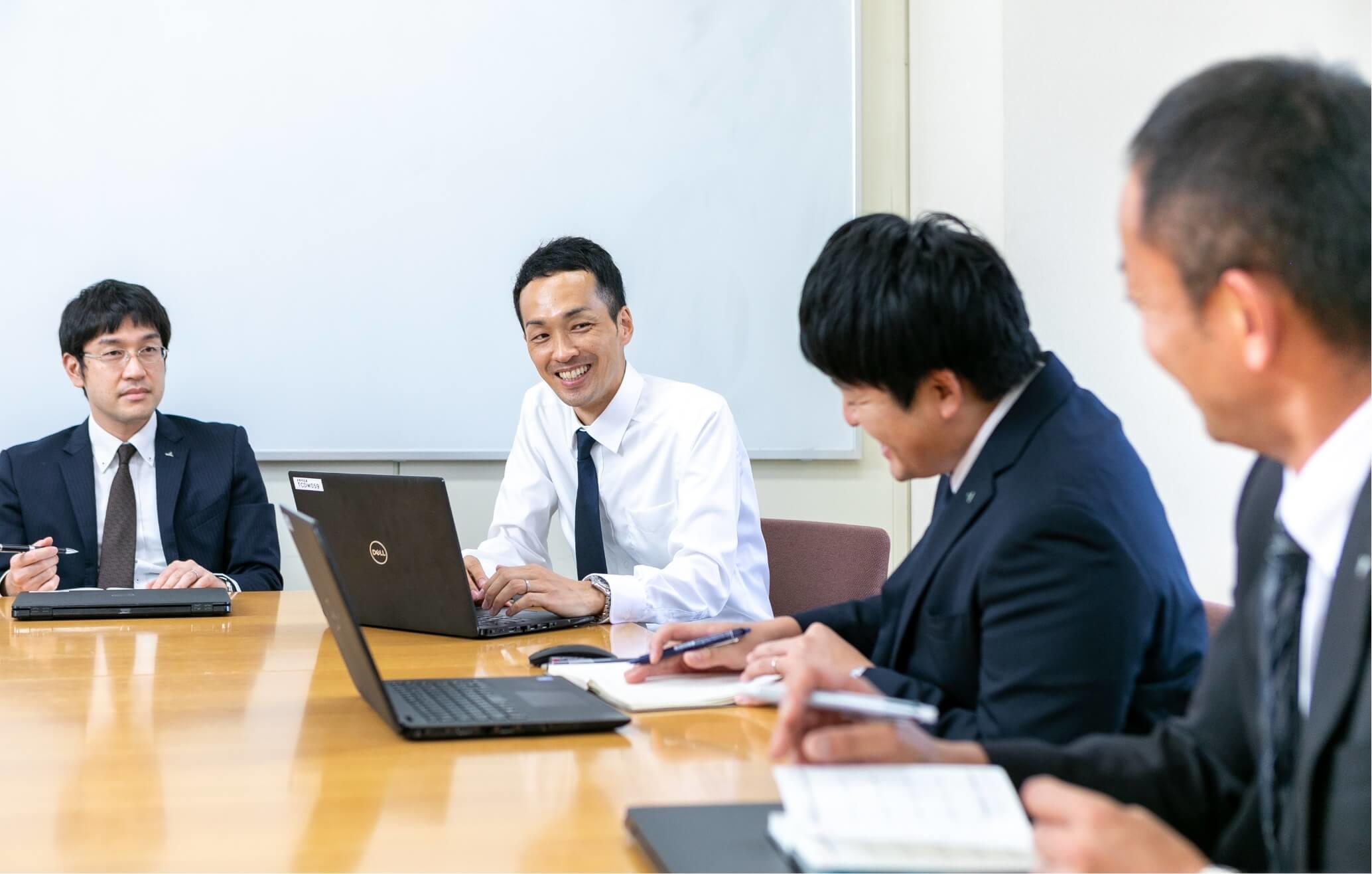 デスクを囲み、パソコンをみながら月時会議をしている長野県信連の男性職員4名