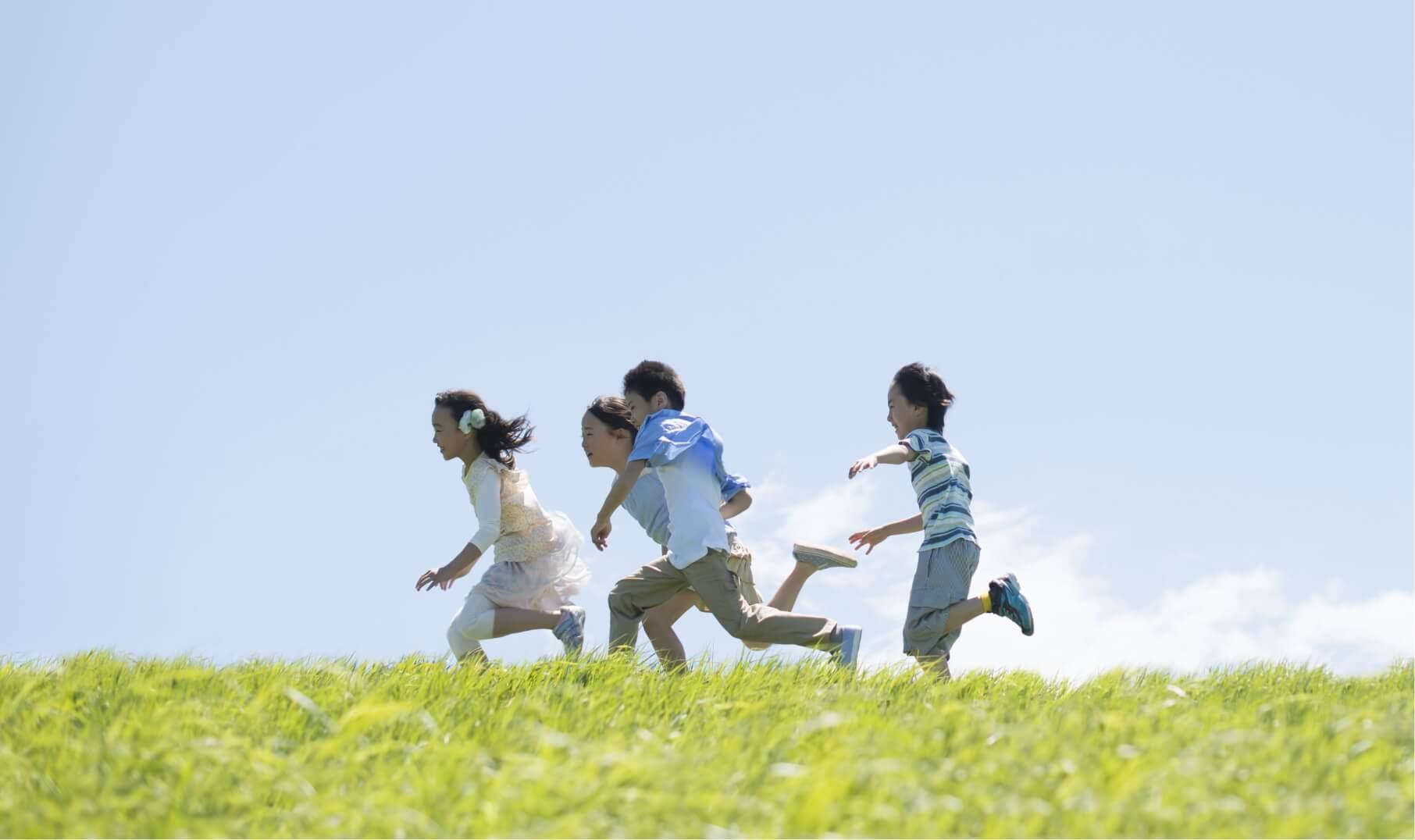 青空の下で野原を走る子ども4名