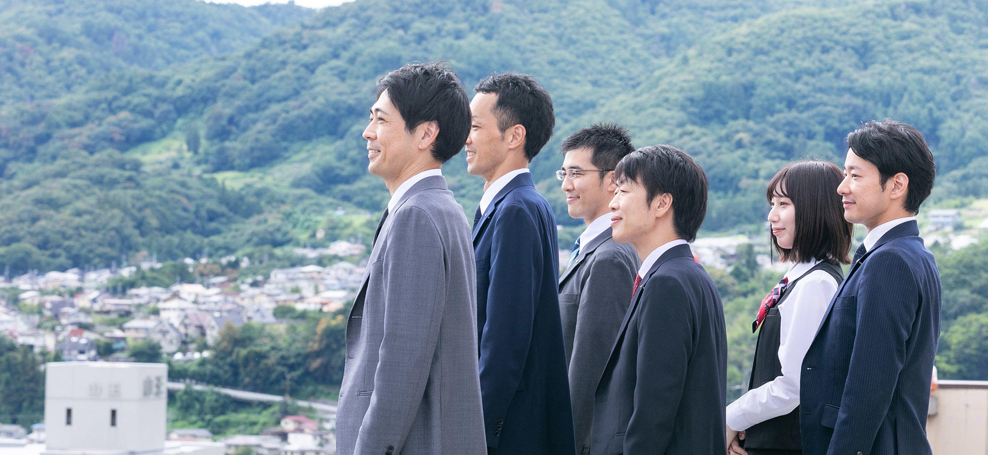 山並みを背景に、長野市街地を望む長野県信連の男性職員5名と女性職員1名の左横顔