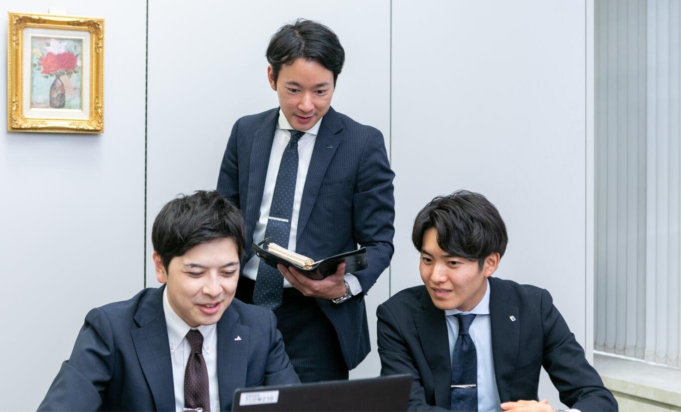 パソコンを見ながら会議をしている長野県信連男性職員3名
