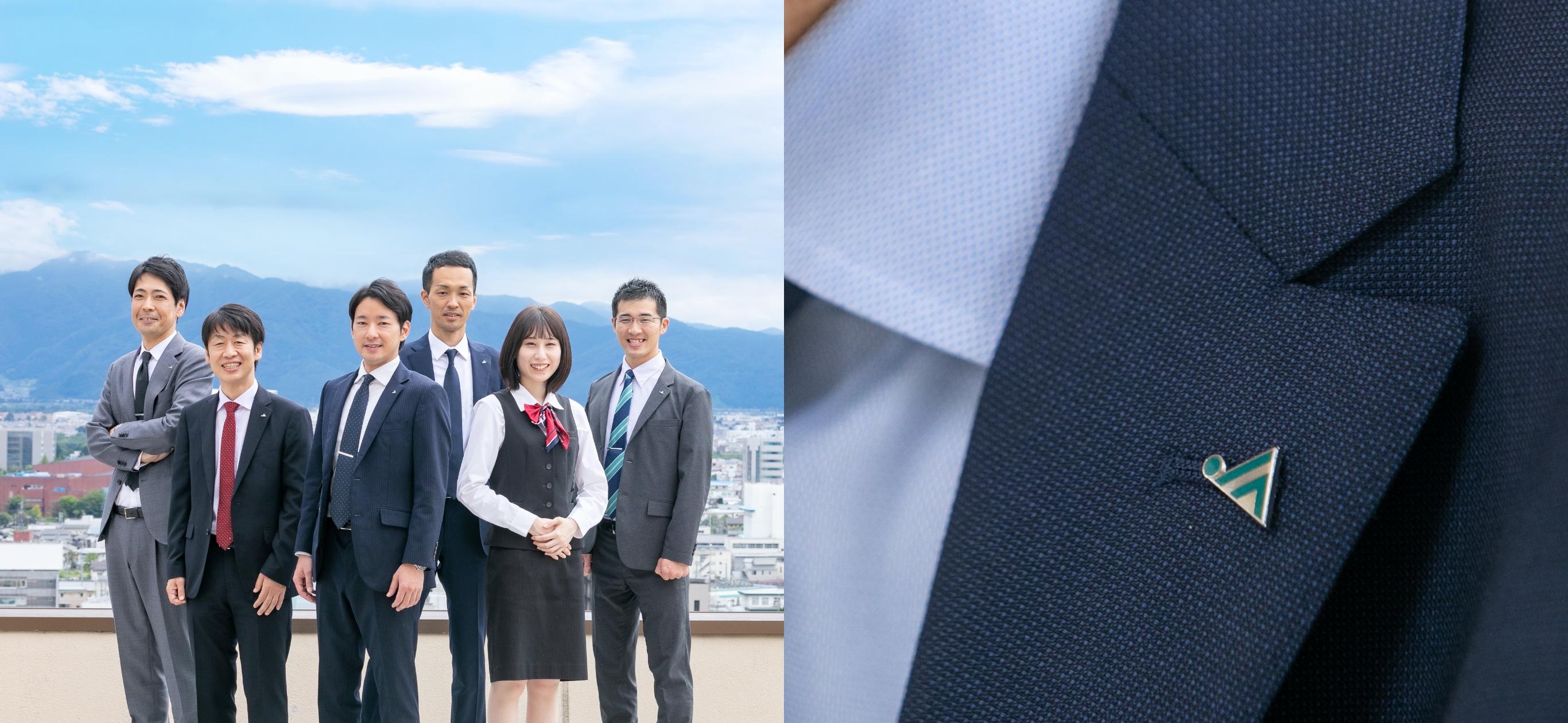 青空を背景に立つ長野県信連職員男性5名と女性1名写真とジャケットの襟にとめたJAバッチ